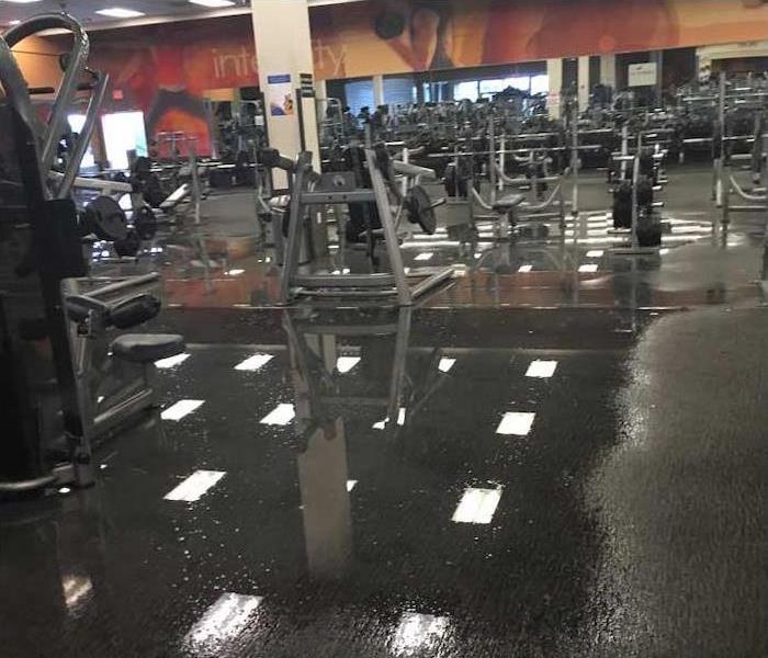 pooling water reflecting lights off fitness center floor with equipment visible