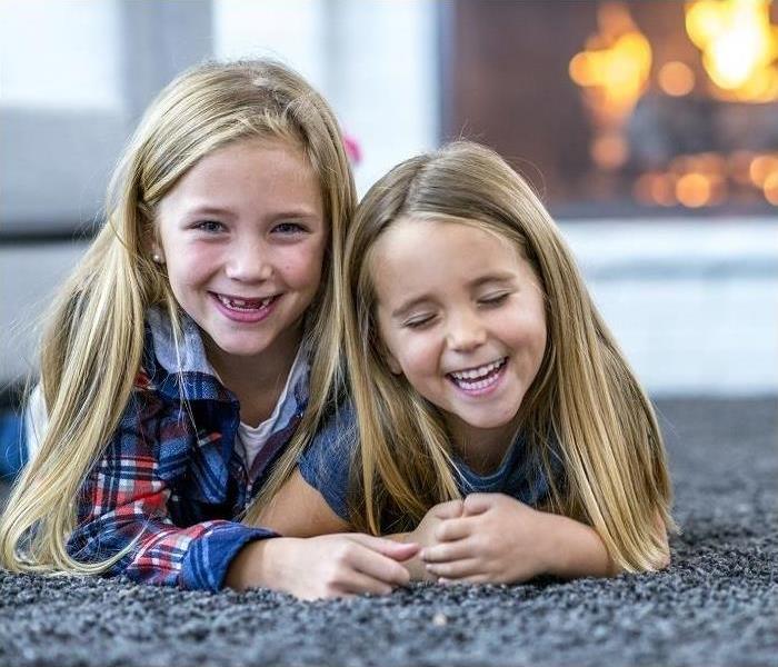 Two girls lying on carpet; fireplace in background.