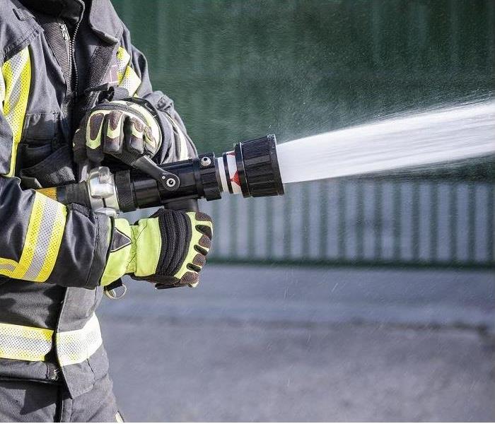 Closeup of fireman’s hand using a hose and water to extinguish fire.